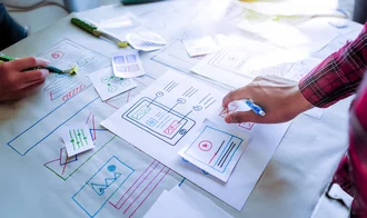 Webdesign Personen arbeiten mit bunten Skizzen und Papierprototypen an einem UI-/UX-Design für eine mobile Anwendung