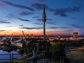 Abendliche Skyline von München mit Olympiapark, Olympiaturm und BMW-Vierzylinder bei Sonnenuntergang – ikonische Stadtansicht mit moderner Architektur und urbaner Atmosphäre