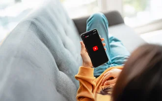 YouTube SEO Frau entspannt auf Sofa mit Smartphone in der Hand, öffnet YouTube-App – Video-Streaming im Alltag