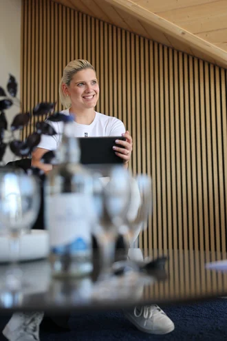 Teresa Schmid von Denkströme sitzt im Besprechungsraum und hält ein Tablet in den Händen; im Vordergrund stehen unscharf Wasserflasche und Gläser auf dem Konferenztisch.