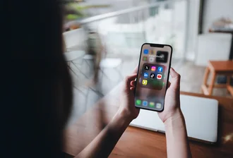 Social Media Plattformen Person hält Smartphone mit geöffnetem Social-Media-Ordner, der Icons von Instagram, Facebook, LinkedIn, TikTok, YouTube, Snapchat und X zeigt – Darstellung digitaler Vernetzung und mobiler Mediennutzung