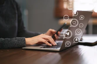 Social Media Marketing Person tippt auf einem Laptop und hält ein Smartphone, umgeben von digitalen Symbolen für Likes, Nachrichten und Follower