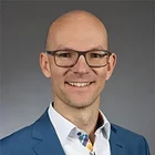 Porträt von Andreas Nietsch im blauen Business-Anzug und Brille vor neutralem Hintergrund – zufriedener Kunde