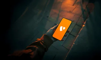 TYPO3 CMS Hand hält Smartphone mit orangefarbenem Bildschirm und TYPO3-Logo, fotografiert bei Dämmerlicht auf dunklem Gehweg – symbolisiert Content-Management, Webentwicklung und mobile CMS-Nutzung
