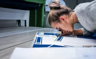 Logo Design Mitarbeiterin prüft sorgfältig einen Druckbogen mit Lupe – Detailaufnahme eines kreativen Produktionsprozesses im Bereich Markenkreation bei der Denkströme