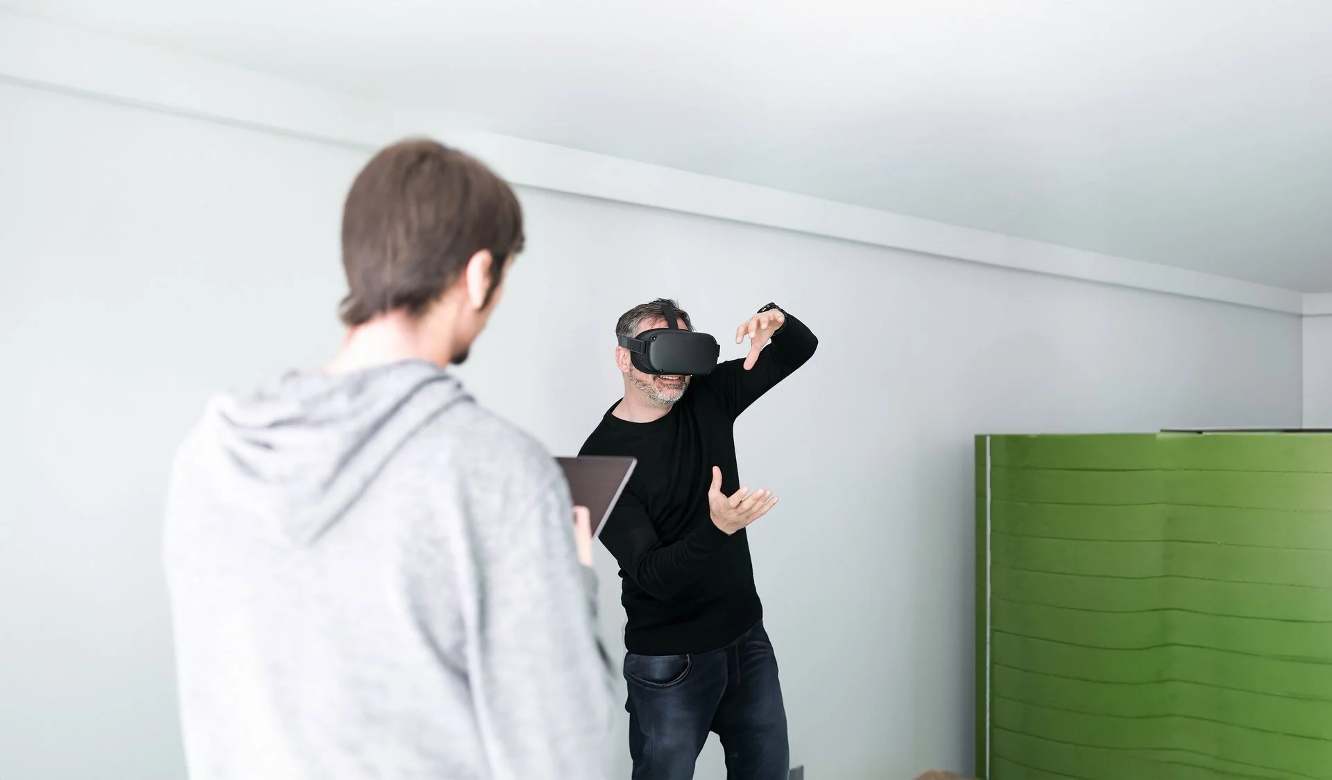 WE CREATE<br/>BRAND LEADER Denkströme IT-Entwickler mit VR-Brille testet virtuelle Realität im Büro der Denkströme Gruppe, betreut von Kollege mit Tablet – Symbol für innovative Digitalentwicklung und immersive Technologien