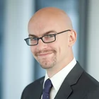 Christian Jakob im Anzug mit Namensschild – professionelles Business-Porträt eines Verwaltungsleiters im modernen Büro