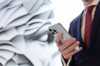 Interimsmanagement Denkströme Mitarbeiter im Anzug nutzt iPhone zur digitalen Kommunikation vor abstrakter Markenwand der Denkströme Gruppe – Symbol für Digital Development und strategische Digitalisierung