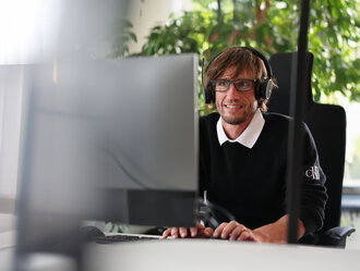 Digitalisierung Mitarbeiter bei Denkströme arbeitet mit Headset am Computer; im Hintergrund sind Pflanzen am Fenster zu sehen.