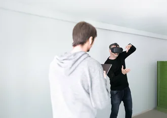 Technologieberatung Denkströme IT-Entwickler mit VR-Brille testet virtuelle Realität im Büro der Denkströme Gruppe, betreut von Kollege mit Tablet – Symbol für innovative Digitalentwicklung und immersive Technologien