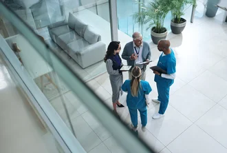 Smart Hospital Multidisziplinäres Team aus medizinischem Fachpersonal und Verwaltungskräften im Gespräch in einem modernen Klinikgebäude – symbolisiert Zusammenarbeit, Gesundheitsmanagement und interprofessionellen Austausch im Gesundheitswesen